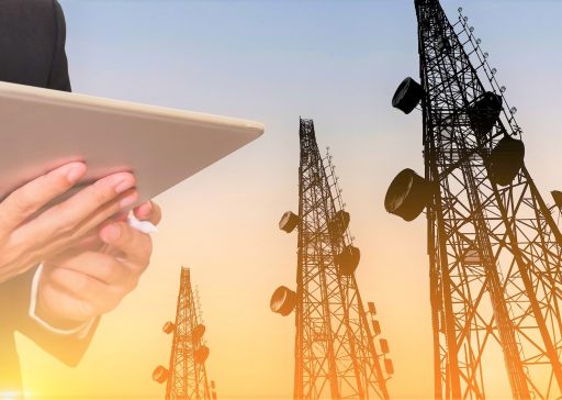 Businessman working on digital tablet, with satellite dish telecom network on telecommunication tower in sunset, telecommunication in business and development